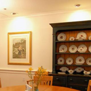 A cozy dining room featuring a china cabinet filled with plates and a wooden table adorned with flowers, complemented by framed artwork on the wall.