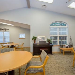 A cozy lounge area with round tables, chairs, a piano, and large windows.
