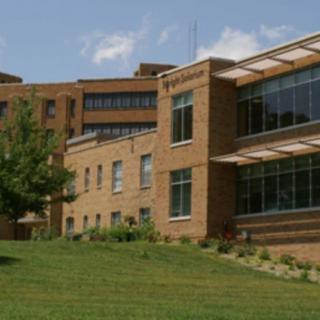 A modern brick building with large windows surrounded by grass and trees.