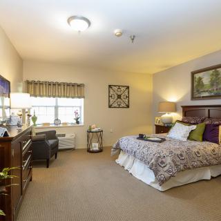 A cozy bedroom with a neatly made bed, wooden furniture, and warm lighting.