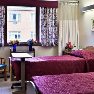 A hospital room with two twin beds, decorated with flowers and curtains, providing a comfortable healthcare environment.