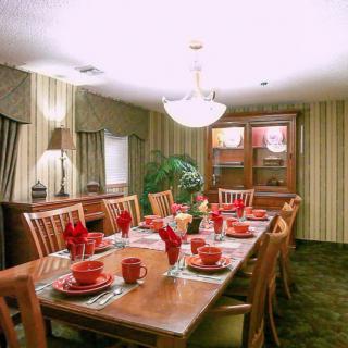 A well-decorated dining room with a large wooden table set for a meal, featuring red dinnerware and a central chandelier.