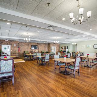 A spacious dining room with wooden floors, multiple tables and chairs, and elegant chandeliers.