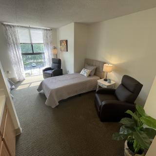 A cozy bedroom with a single bed, armchair, and large window letting in natural light.
