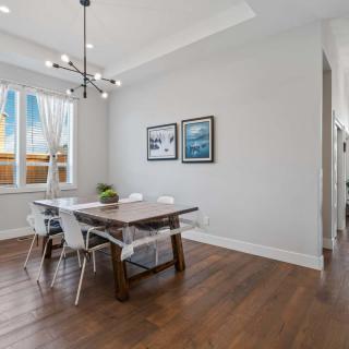 A modern dining room featuring a wooden table, contemporary chandelier, and ample natural light.