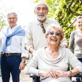 A group of seniors enjoying a day outdoors, with one person in a wheelchair, all smiling and looking content.