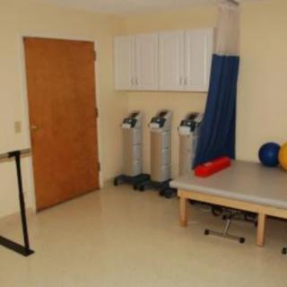 A physical therapy room equipped with exercise machines and a therapy table.