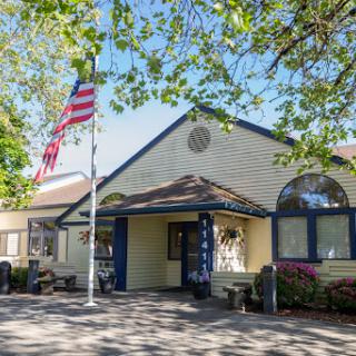 A charming community center with an American flag waving in front, surrounded by lush greenery.