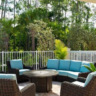 An inviting outdoor patio with wicker furniture and blue cushions, surrounded by lush greenery.
