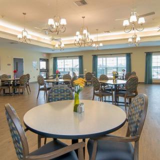 A spacious dining area with neatly arranged tables and chairs, adorned with chandeliers and natural light from large windows.