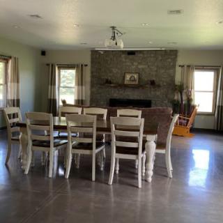 A spacious dining room with a large table and chairs, featuring a stone fireplace and multiple windows.