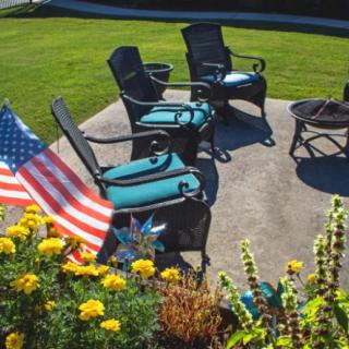 A sunny outdoor patio with chairs, an American flag, and colorful flowers.