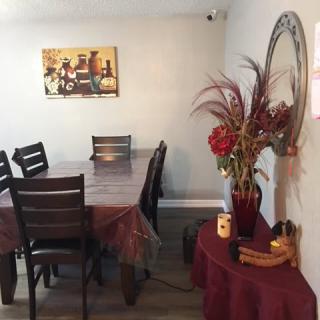 A cozy dining room with a long table, chairs, wall art, and decorative elements such as a mirror and vase with flowers.