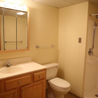 A clean and simple bathroom featuring a toilet, sink, mirror, and shower.