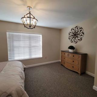A modern bedroom with a chandelier, dresser, and a large window.