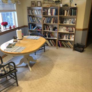 A cozy reading room with a wooden table, chairs, and a large bookshelf filled with books.