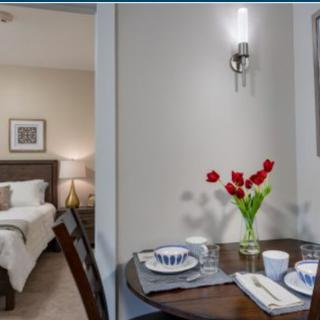A cozy apartment interior featuring a dining table with a floral centerpiece and a view into the bedroom.