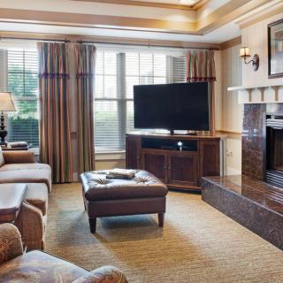 A cozy living room with a television and fireplace, featuring comfortable seating and large windows.