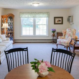 A cozy living room with a dining area, featuring comfortable seating and a flower vase on the table.