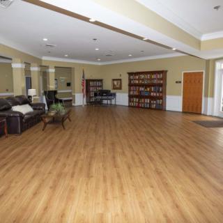 A spacious room with wooden floors, featuring a sofa, a bookshelf, and a piano.