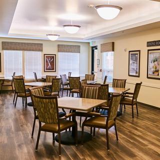 A well-lit dining room with multiple tables and chairs arranged on a wooden floor.