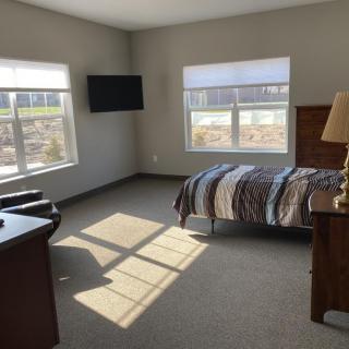 A minimalist bedroom with a single bed, television, and ample sunlight streaming through the windows.