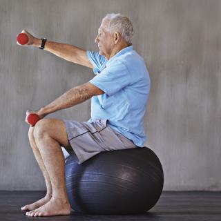 A senior man exercises with dumbbells while sitting on a balance ball.