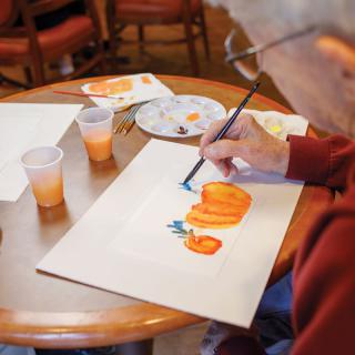 A senior individual painting pumpkins using watercolors at a table.
