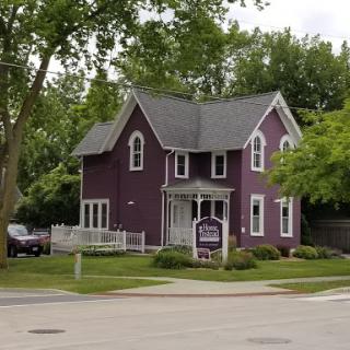 A charming two-story purple house surrounded by greenery in a residential neighborhood.