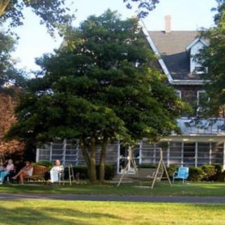 A large house with a lawn and outdoor seating area, featuring chairs and a swing.