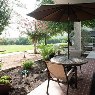 Outdoor patio area with a table, chairs, and an umbrella in a garden setting on a sunny day.