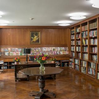 A cozy library room with wooden bookshelves and a central table adorned with flowers, creating an inviting atmosphere for reading and study.