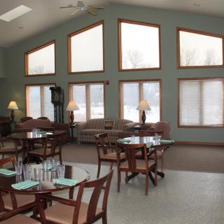 A spacious dining area with multiple tables and chairs, large windows, and cozy lighting.
