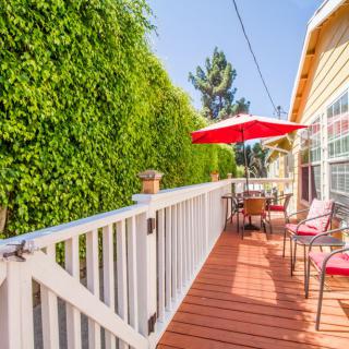 A sunny outdoor deck with chairs and an umbrella, bordered by a tall hedge.