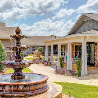 A serene outdoor space featuring a beautifully designed fountain surrounded by well-maintained gardens and residential architecture.