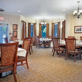 An elegant dining room with neatly arranged tables and chairs, featuring large windows and a chandelier.