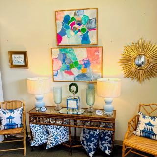 A beautifully decorated living room with colorful abstract artwork, rattan chairs, and elegant table lamps.
