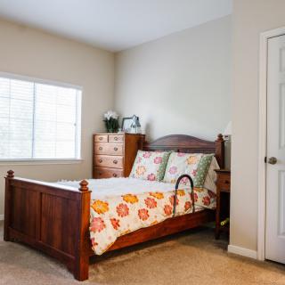 A cozy bedroom with a wooden bed frame, floral quilt, and a window allowing natural light.