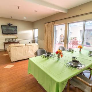 A cozy dining area featuring a green tablecloth, flowers, and an inviting living room in the background.