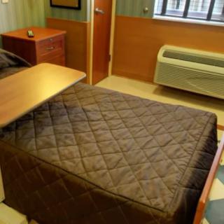 A small hospital room featuring a single bed with a quilt, a side table, and a window.