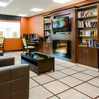 A modern office interior featuring comfortable seating, bookshelves, computer desks, and a wall-mounted television.