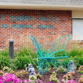 A turquoise butterfly sculpture surrounded by colorful flowers in front of a brick building.