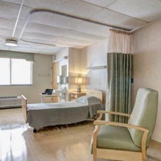 A clean and well-lit hospital room with a bed and chair, designed for patient care.