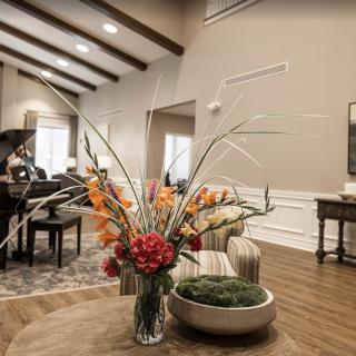 A modern living room with a high ceiling featuring elegant furniture and a vibrant floral arrangement on a wooden table.