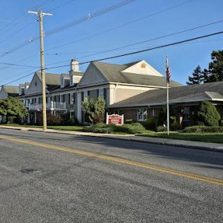 A hotel situated along a quiet street, surrounded by greenery and under a clear blue sky.