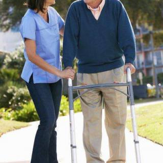 A caregiver assists an elderly person using a walker outdoors.
