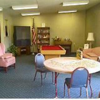 A cozy room with various furniture, including chairs, a table, a television, and a bookshelf.