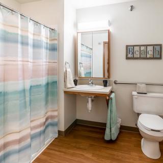 A clean and well-organized bathroom with a colorful shower curtain and wooden flooring.