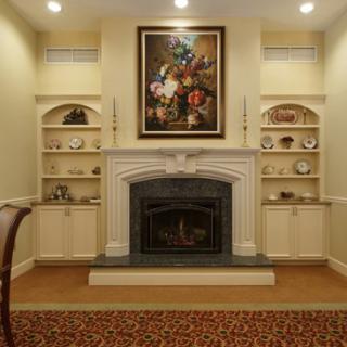 A cozy living room featuring a decorative fireplace, built-in shelves, and a beautiful floral painting.