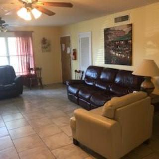 A cozy living room featuring leather sofas, an armchair, and a ceiling fan with tiled flooring.